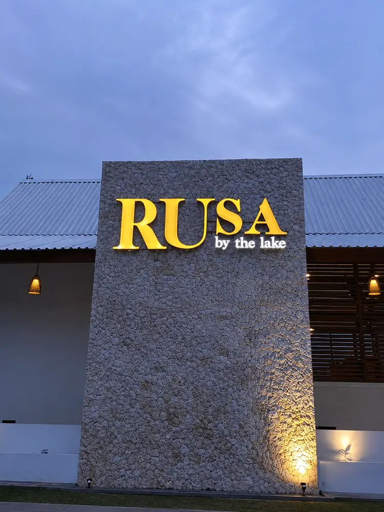 Illuminated Rusa by The Lake stone entrance signage at dusk.